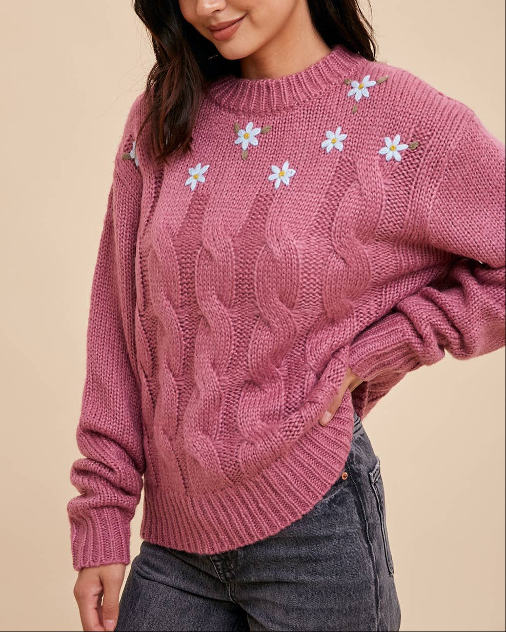 Woman wearing a pink sweater with floral patterns on a beige background