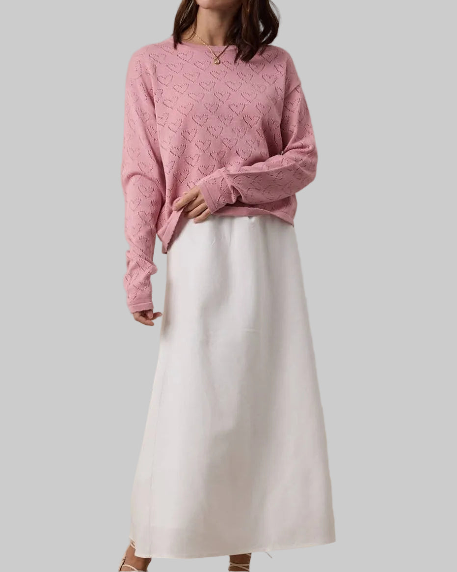 Woman wearing a pink sweater and white skirt against a beige background