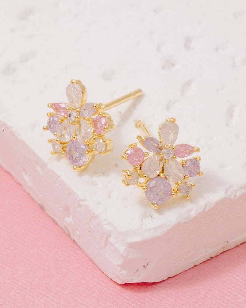 Gold earrings with pink and white stones on a textured white surface