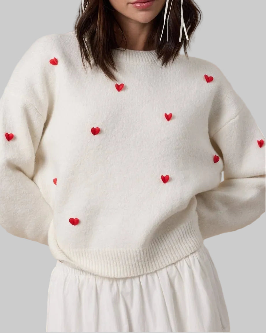 Woman wearing a white sweater with red heart patterns against a beige background