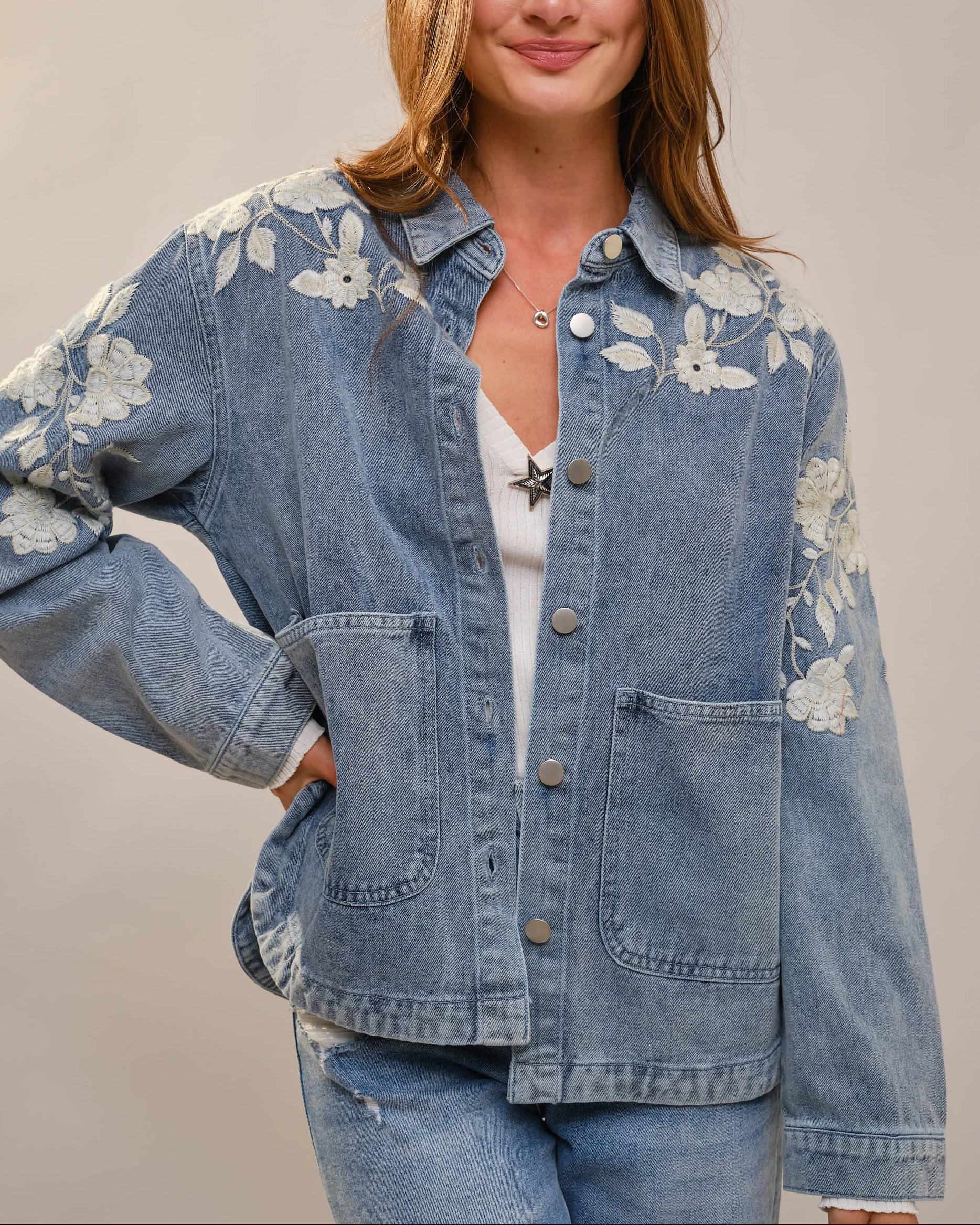 Woman wearing a blue denim jacket with floral embroidery on a plain background