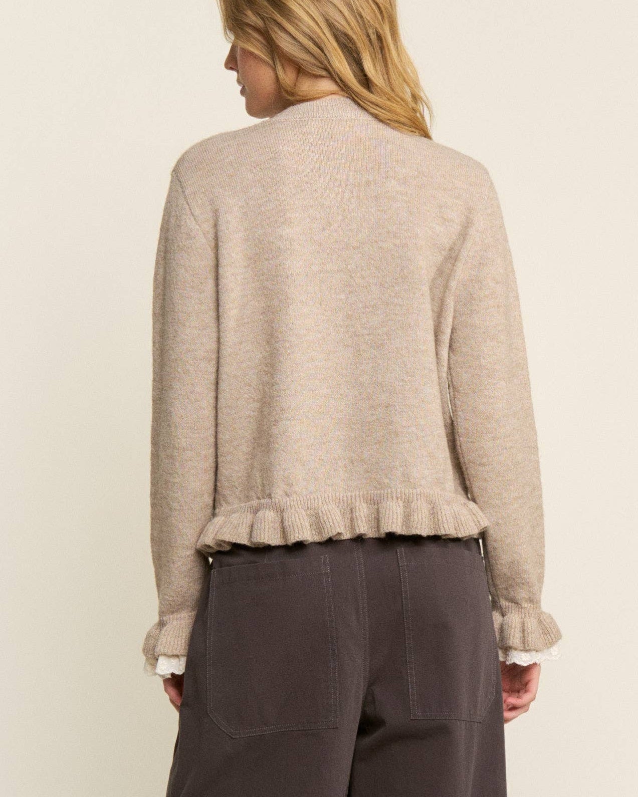 Person wearing a beige cardigan and dark gray pants on a white background