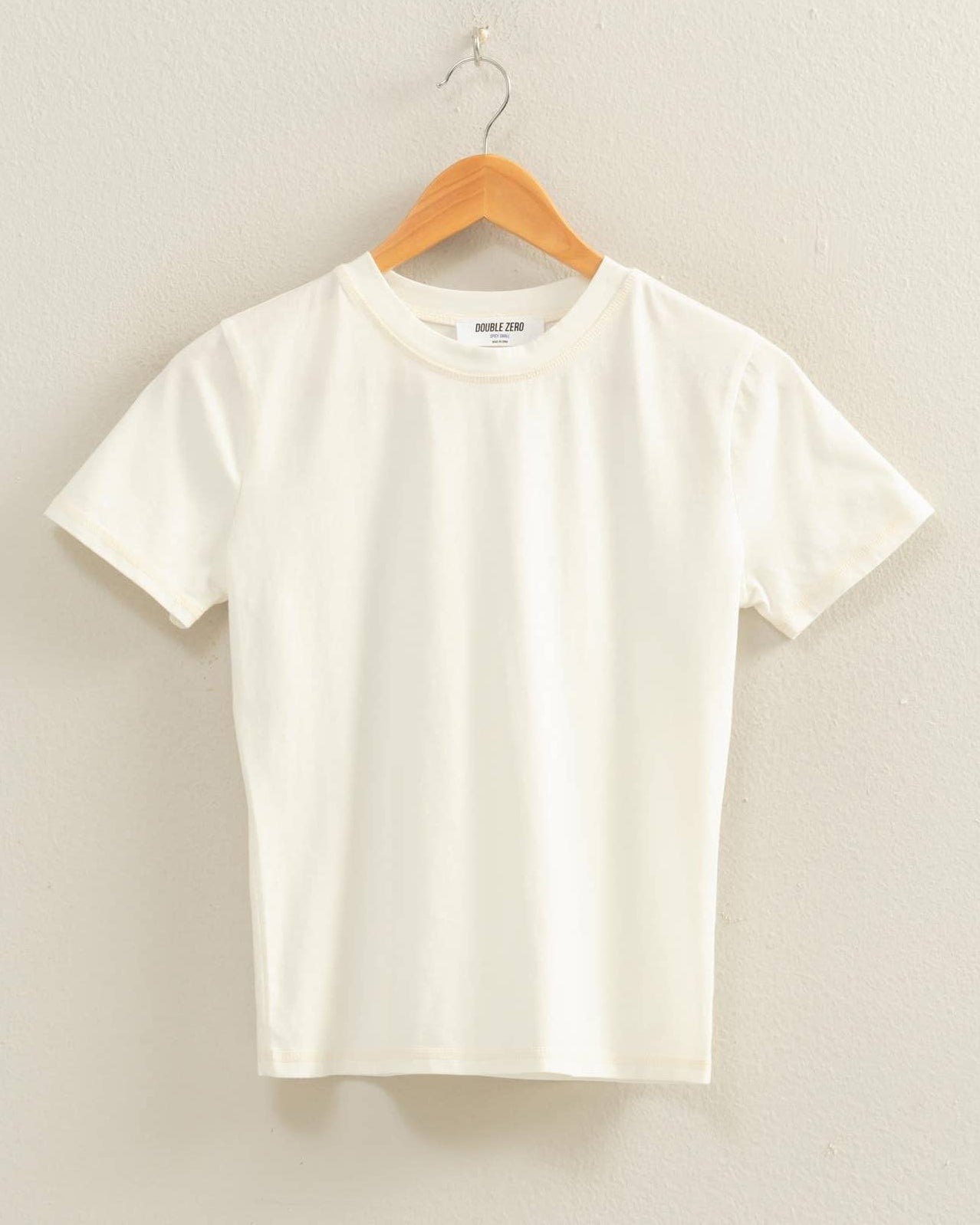 White t-shirt on a wooden hanger against a plain background