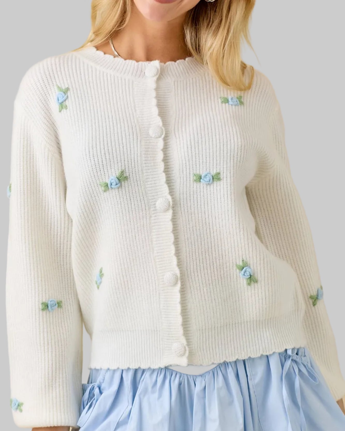 Woman wearing a white cardigan with floral embellishments against a beige background