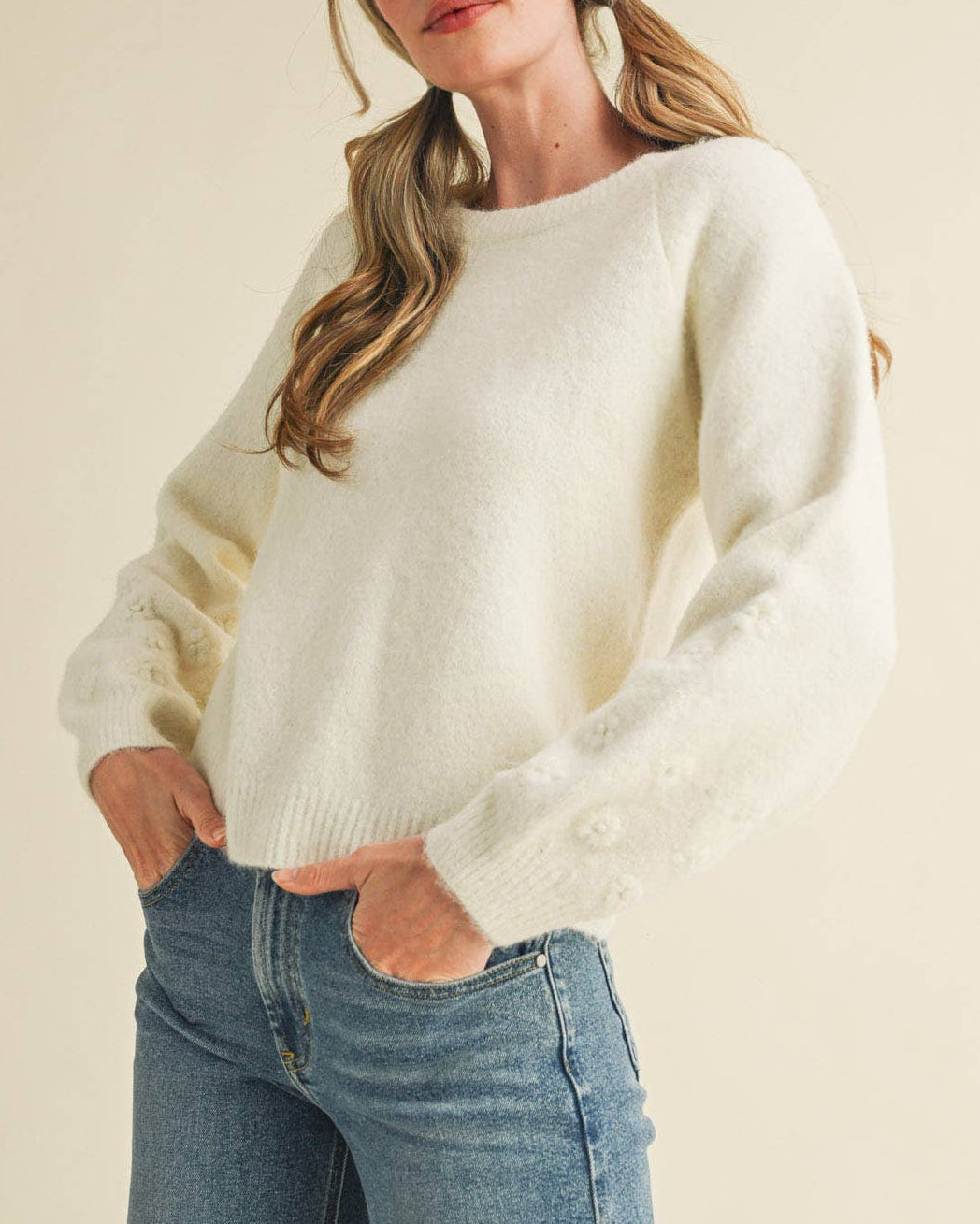 Woman wearing a white sweater and blue jeans against a beige background