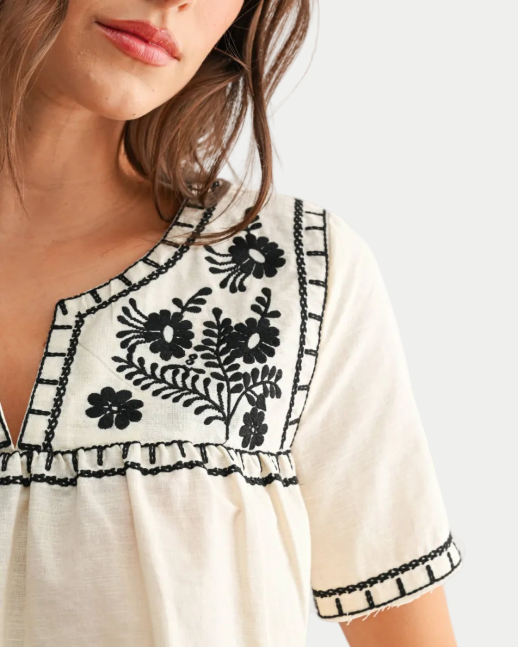 Woman wearing a white dress with black floral embroidery on a plain background close view