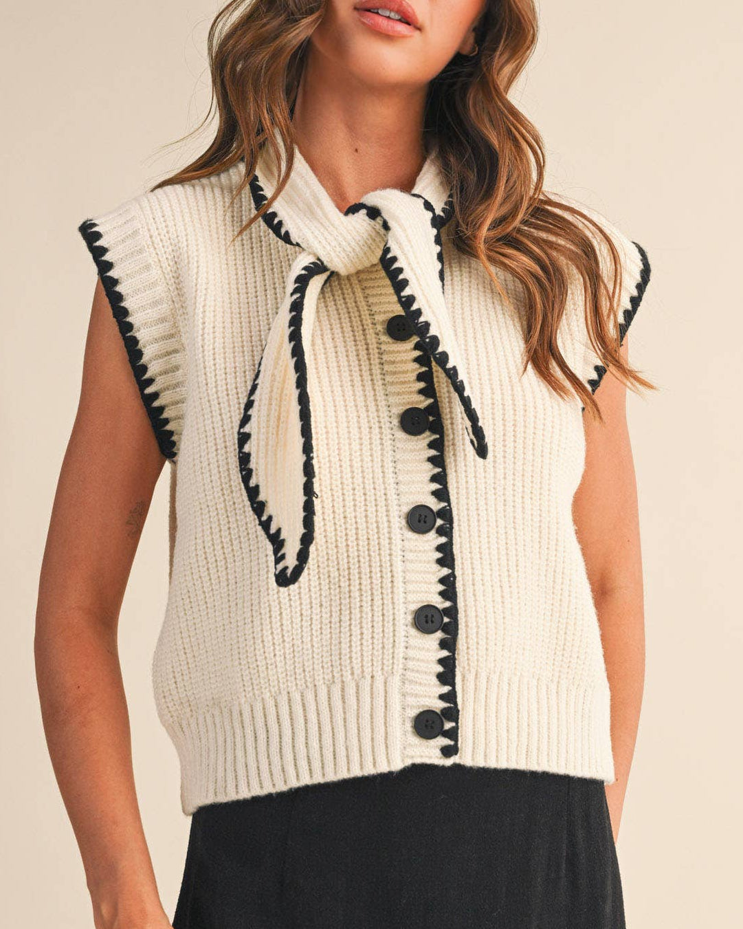 Woman wearing a cream-colored sleeveless knitted vest with black accents on a beige background