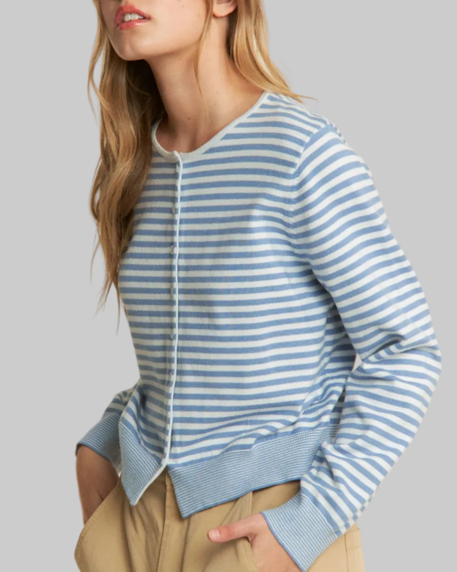 Woman wearing a blue and white striped sweater with beige pants on a plain background