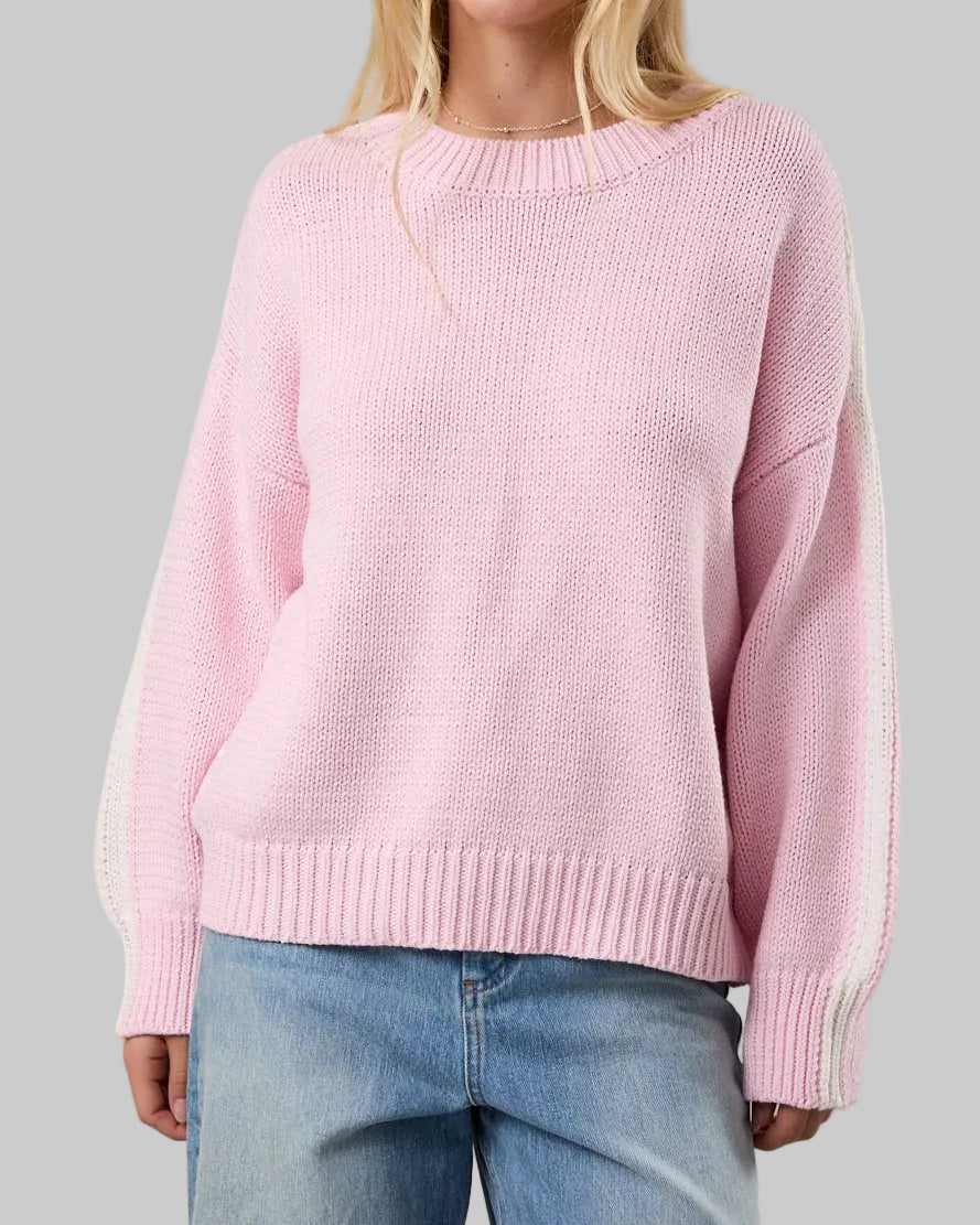 Woman wearing a pink sweater and blue jeans against a plain background