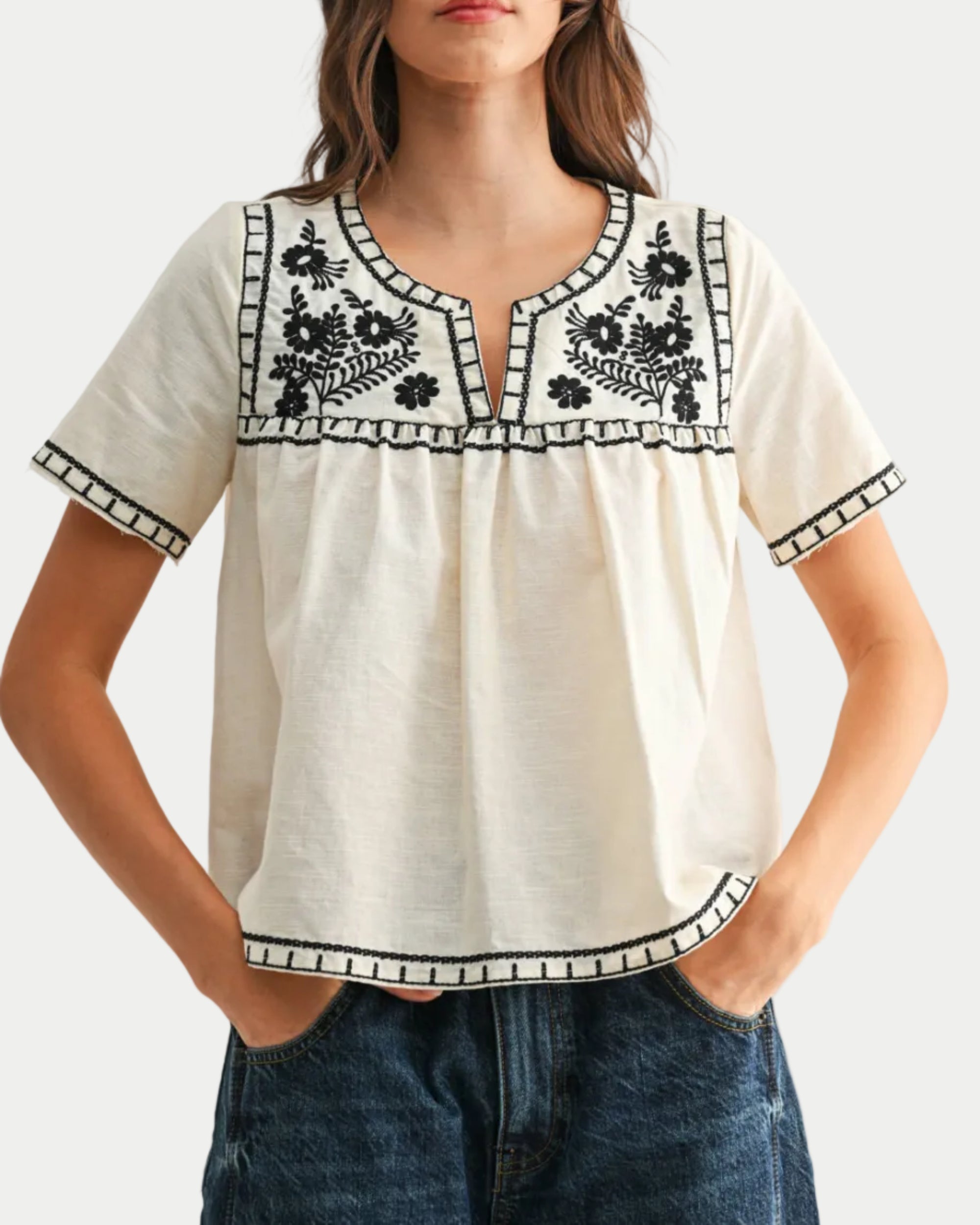 Woman wearing a white blouse with black embroidery and blue jeans on a white background