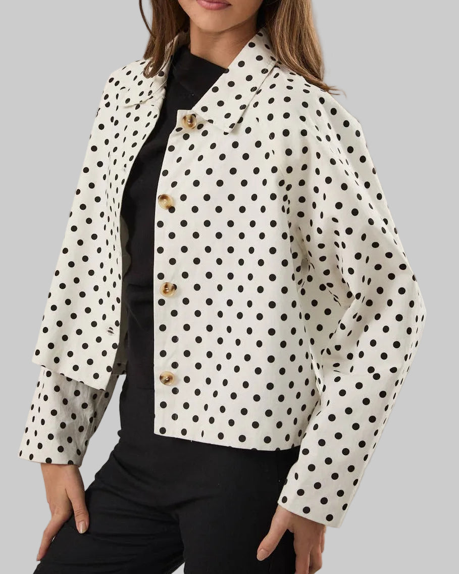 White jacket with black polka dots worn by a person on a neutral background