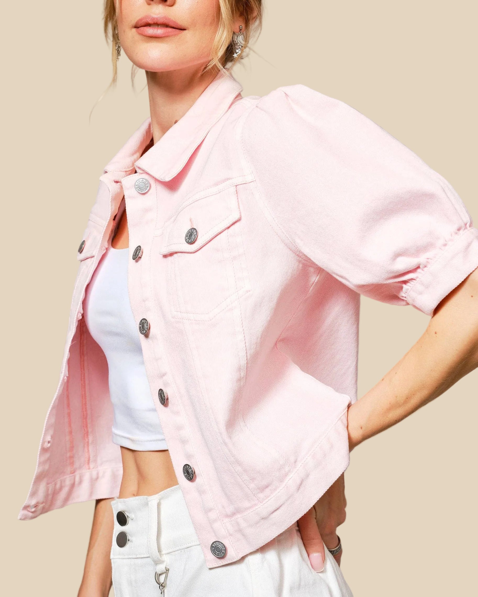 Woman wearing a light pink denim jacket over a white top and pants on a gray background