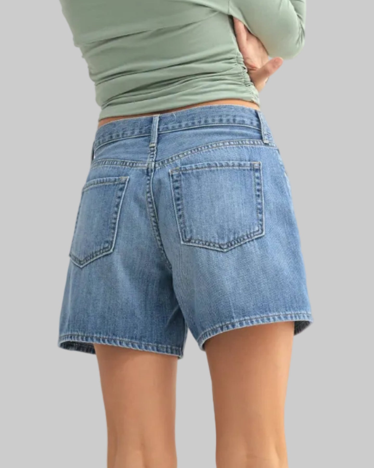 Woman wearing a green off-shoulder top and denim shorts on a white background