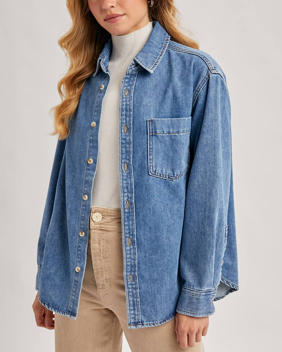 Woman wearing a blue denim shirt over a white turtleneck on a plain background