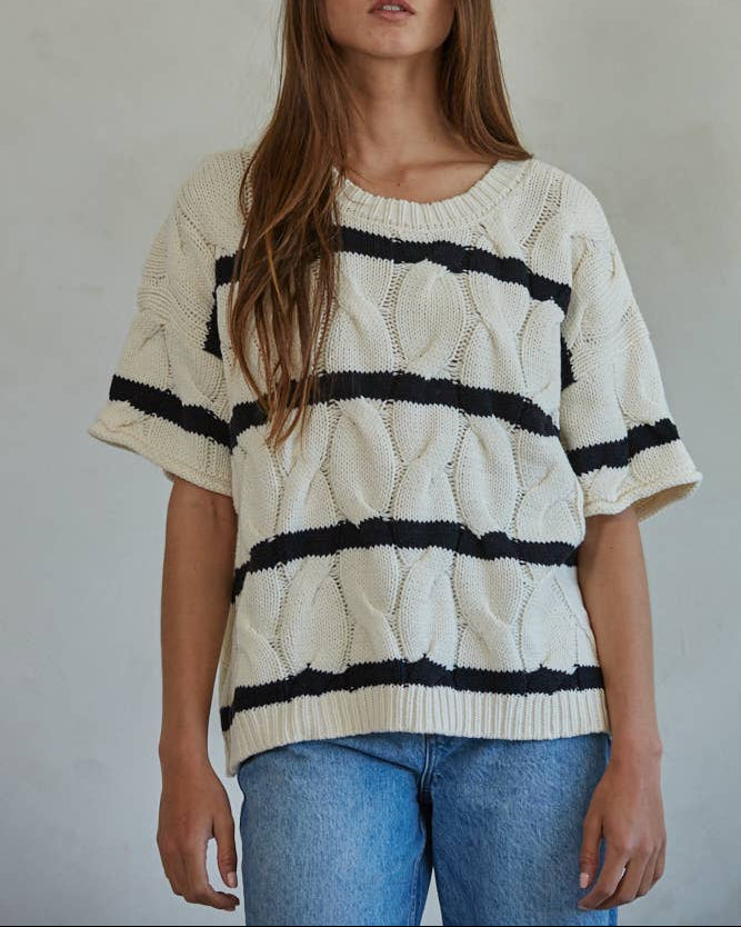 Woman wearing a cream sweater with black stripes and blue jeans against a plain background