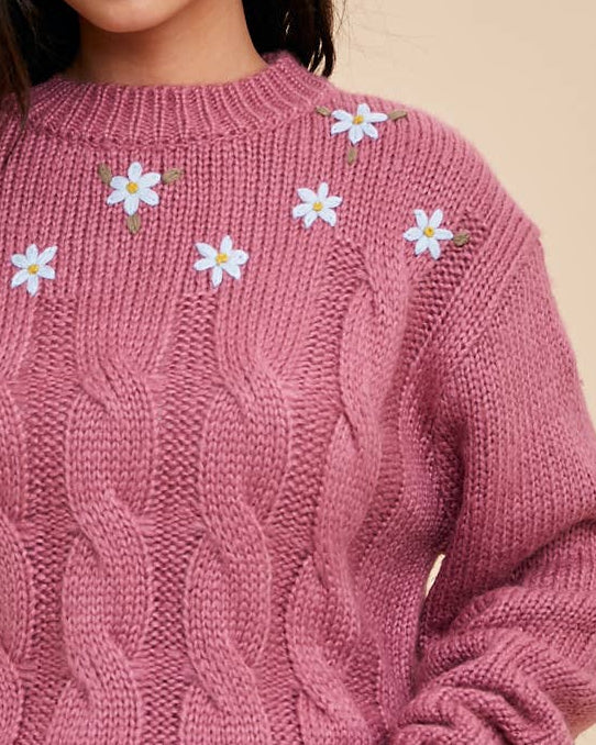 Woman wearing a pink sweater with floral patterns on a beige background
