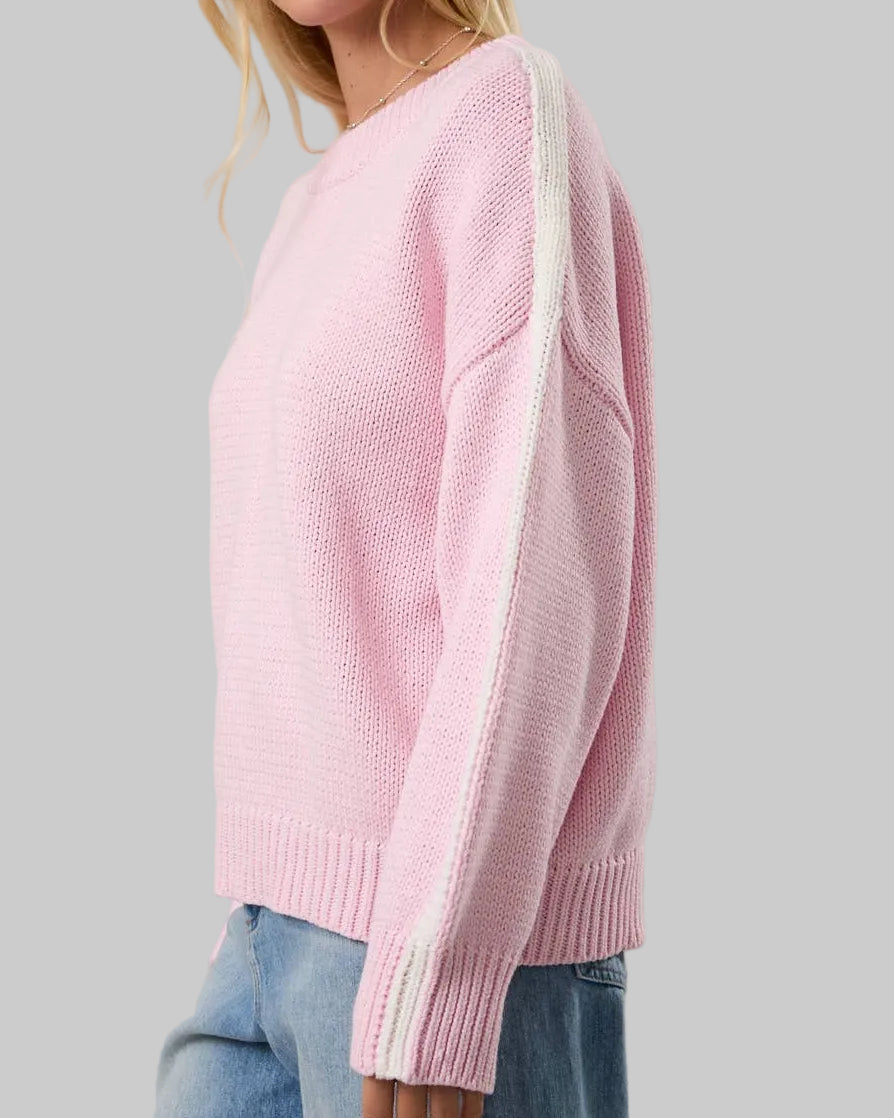 Woman wearing a pink sweater with white stripes on a plain background