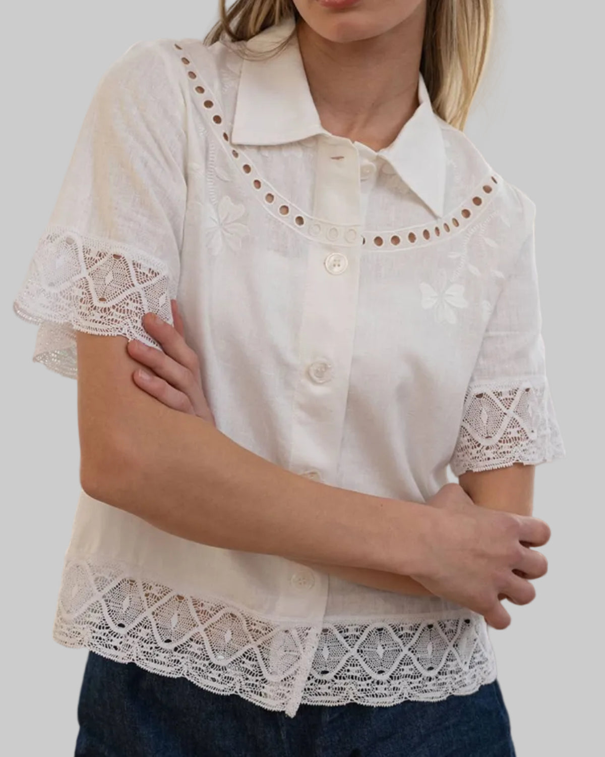 Woman wearing a white lace-trimmed blouse and denim shorts in a softly lit room.
