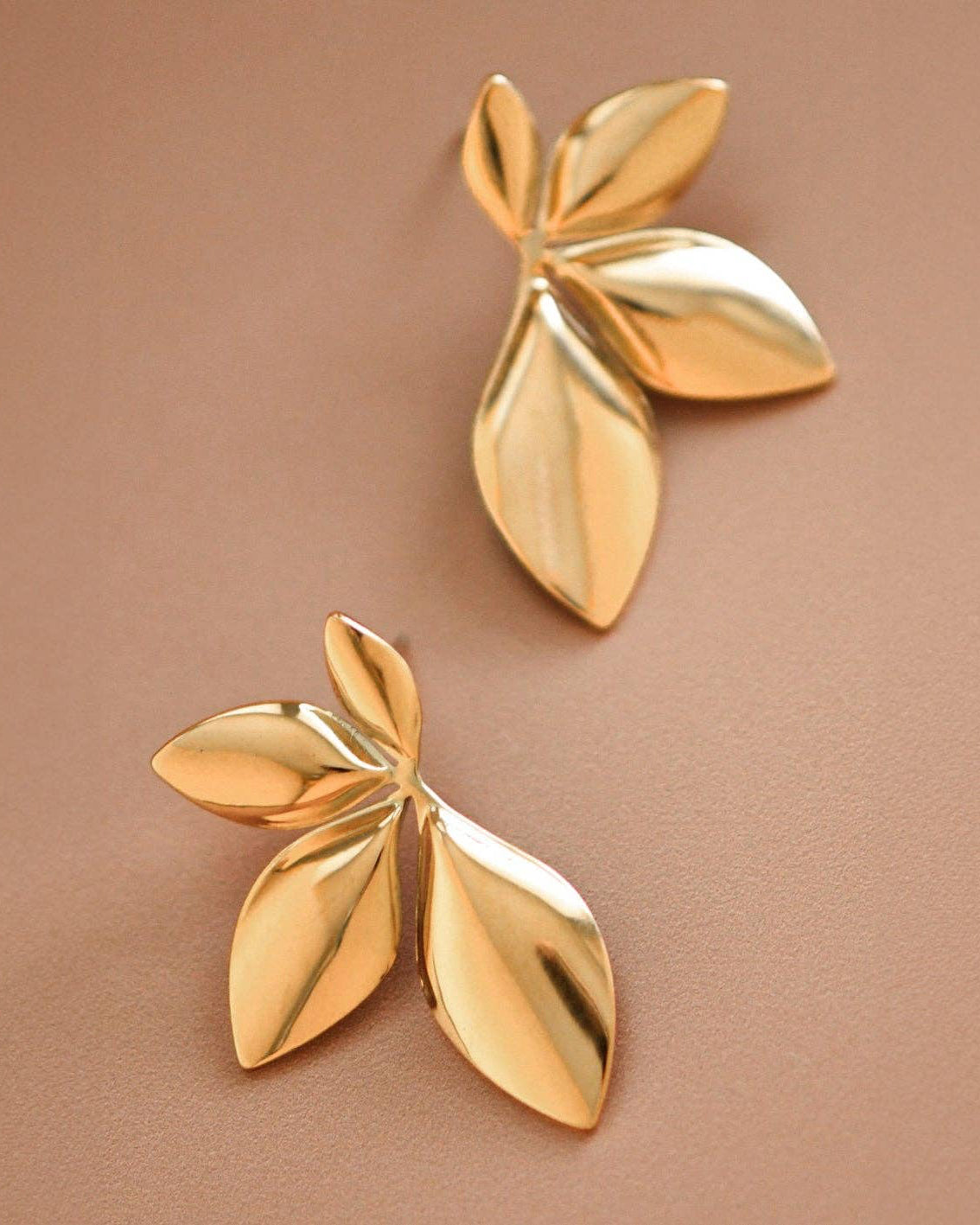 Pair of gold leaf-shaped earrings on a brown background