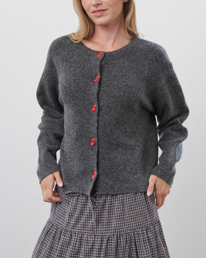 Woman wearing a gray cardigan with red buttons in a bright room.