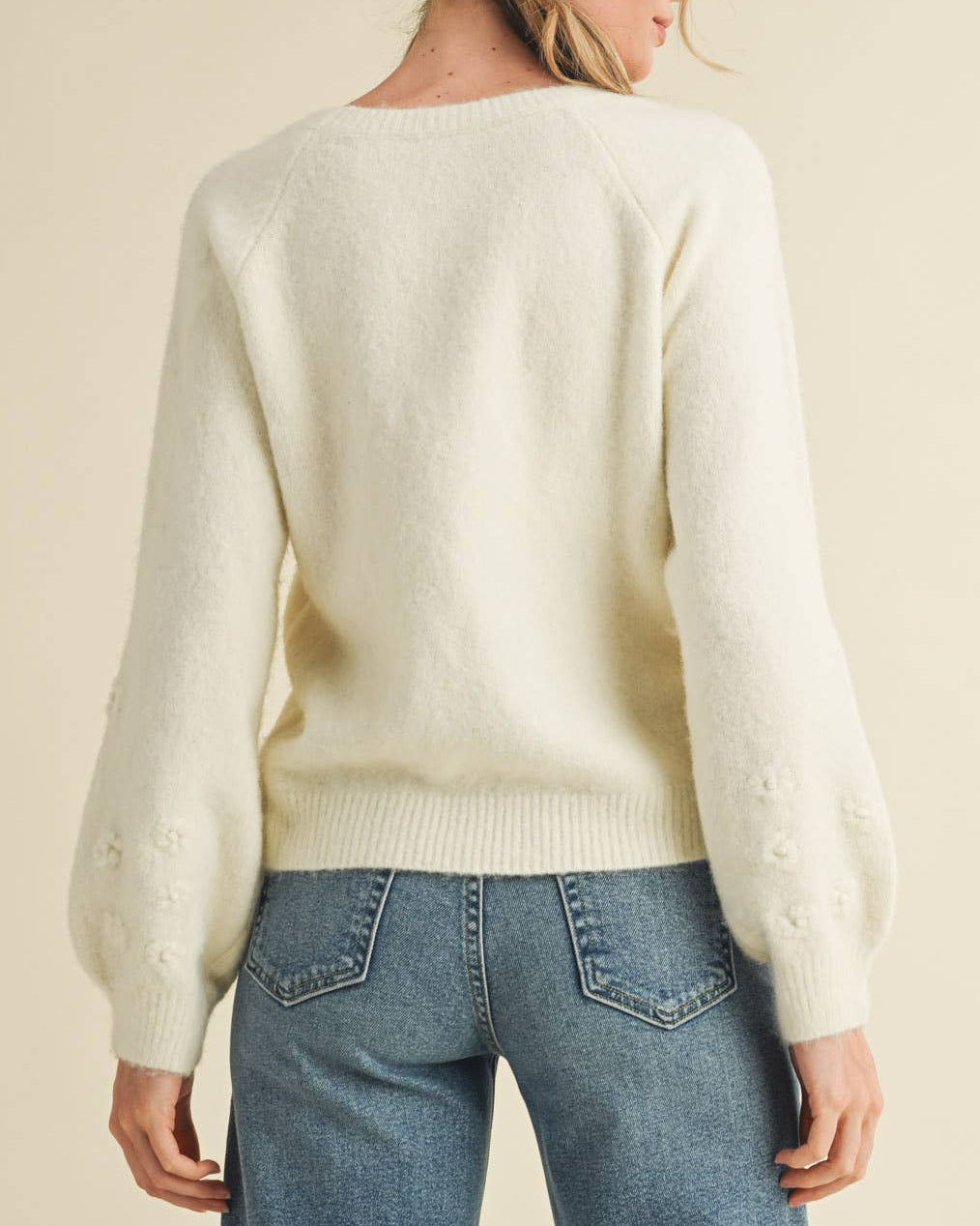 Woman wearing a cream sweater and blue jeans against a beige background